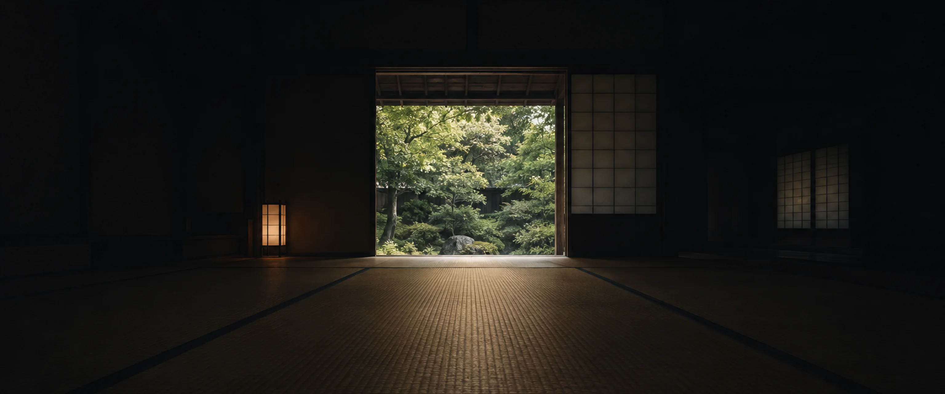 Una sala de tatami en penumbra que se abre a un jardín iluminado, con una lámpara de papel encendida en un rincón